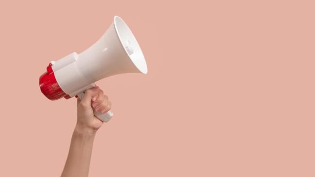 Eine Person hält ein Megafon vor einem pinken Hintergrund. (Link zur Seite Öffentliche Bekanntmachungen)