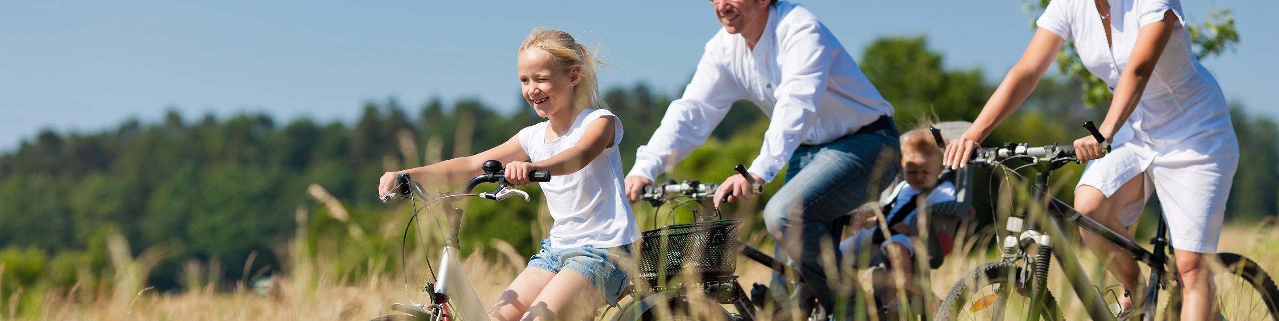 Eine Familie genießt eine Fahrradtour in der Natur, umgeben von Bäumen und Wiesen.