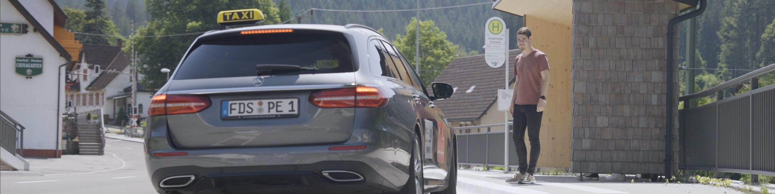 Ein Taxi hält vor einem Jungen, der auf dem Gehweg an einer Bushaltestelle wartet